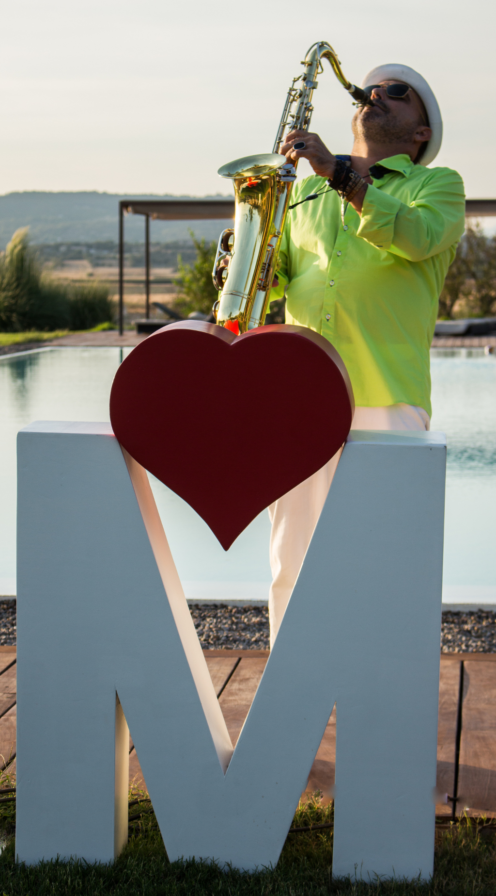  Imágen retrato del músico saxofonista Moisax en una escena donde se puede apreciar el verde de la naturaleza, el elegante blanco de la ropa y el rojo intenso que asocia música y corazón